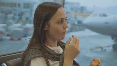 Joven-come-mandarina-en-el-aeropuerto-con-el-avión-en-el-fondo