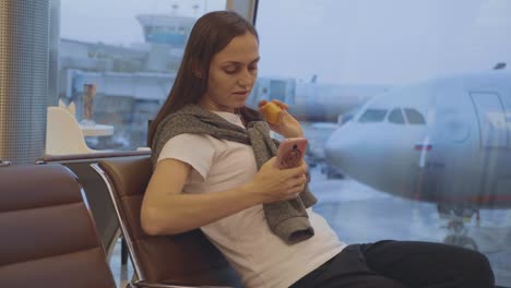 Young-woman-eats-tangerine-at-airport-with-airplane-on-the-background