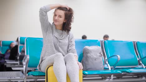 Cheerful-and-happy-young-woman-is-sitting-on-her-luggage-and-laughing