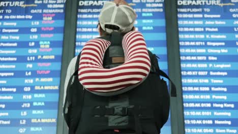 Backpacker-checking-flight-information-on-digital-schedule-display-in-iairport