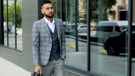 A-young-handsome-businessman-student-in-a-suit,-comes-with-a-briefcase,-at-the-station,-at-the-airport-or-business-center