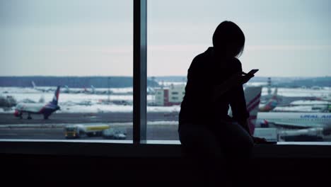 Frau-im-Flughafen-terminal-warten-auf-Flug-mit-smartphone