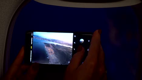 Close-up-woman-hand-holding-mobile-phone-and-take-a-photo-outside-airplane-window