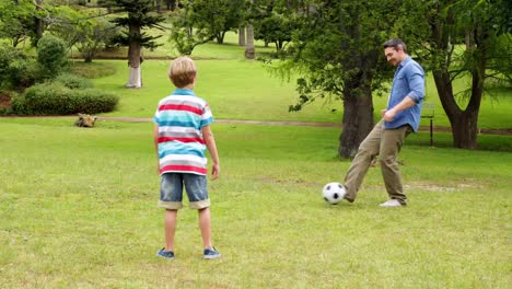 Father-and-son-kicking-football-back-and-forth-in-park