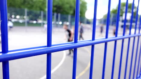Kinder-spielen-Fußball-hinter-einem-Metall-Zaun