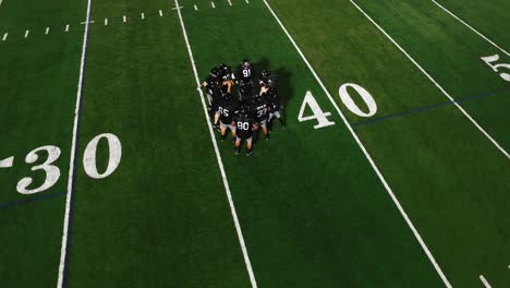 The-camera-spins-from-above-as-a-football-team-in-a-huddle-gets-hyped-before-a-game