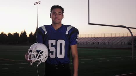 Portrait-of-a-football-player-on-a-field-holding-his-helmet