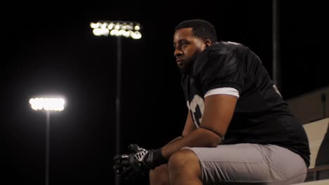 Pan-down-of-a-football-player-sitting-on-the-sidelines-watching-his-team