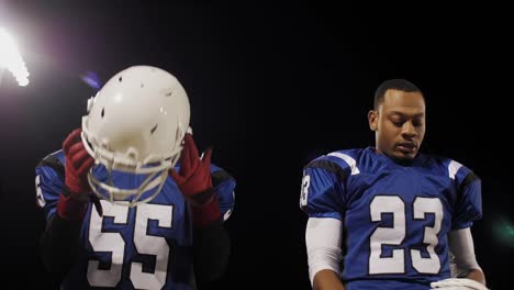 Two-football-players-putting-on-their-helmets-and-walking-onto-the-field