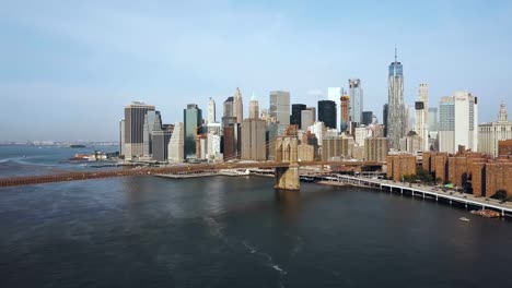 Aerial-view-of-the-capital-of-America,-New-York.-Drone-flying-up-to-the-Brooklyn-bridge-through-the-East-river