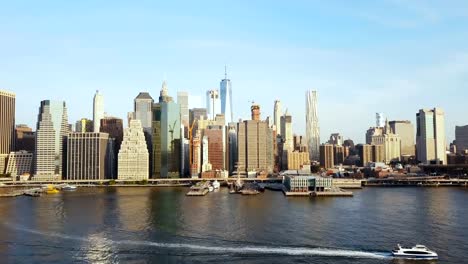 Aerial-view-of-famous-city,-New-York,-America.-Drone-flying-over-the-East-river-with-boat-riding-through-and-Manhattan