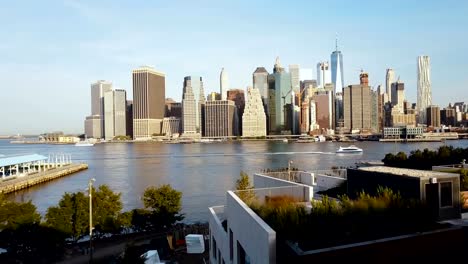 Aerial-view-of-young-woman-standing-on-the-pier-in-Brooklyn-park,-drone-flying-to-Manhattan-in-New-York,-America