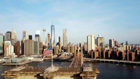 Vista-aérea-del-puente-de-Brooklyn-con-la-bandera-americana-ondeando-en-el-viento.-Vista-panorámica-del-río-del-este,-Manhattan-en-Nueva-York