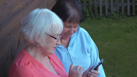 Two-elderly-woman-browsing-mobile-phone-together-in-countryside-garden