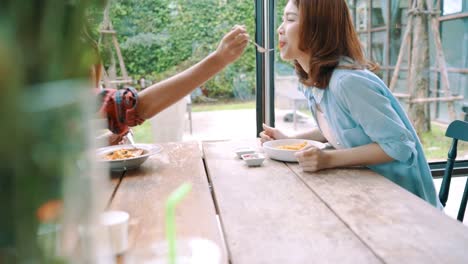 Beautiful-happy-Asian-women-lesbian-lgbt-couple-sitting-each-side-eating-a-plate-of-Italian-seafood-spaghetti-and-french-fries-at-restaurant-or-cafe-while-smiling-and-looking-at-food.