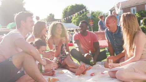 Grupo-de-amigos-comiendo-y-bebiendo-como-se-sientan-en-la-alfombra-en-fete-jardín-de-verano---filmada-en-cámara-lenta