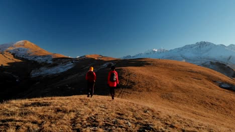 Aerial-view-of-a-two-girls-traveler-with-backpacks-and-cameras-stroll-through-the-hills-between-the-epic-rocks-in-the-mountains.-Girls-photographers-with-their-cameras-at-sunset