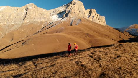 Aerial-view-of-a-two-girls-traveler-with-backpacks-and-cameras-stroll-through-the-hills-between-the-epic-rocks-in-the-mountains.-Girls-photographers-with-their-cameras-at-sunset