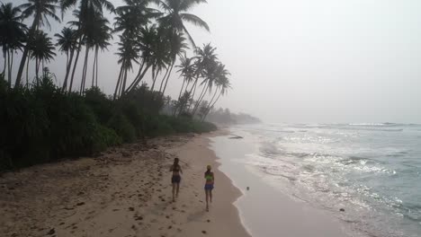 Dos-estilo-de-vida-saludable-jóvenes-amigos-corriendo-en-playa-tropical-durante-salida-del-sol-en-la-mañana,-aerial-drone-ve-imágenes