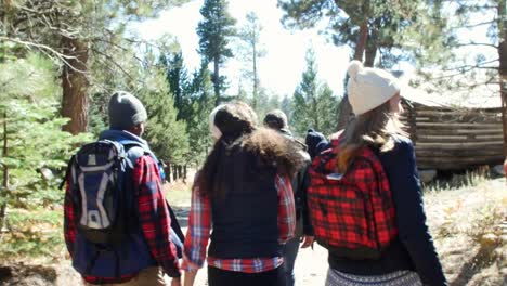 Six-friends-hiking-past-a-cabin-in-a-forest,-back-view,-shot-on-R3D