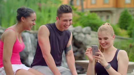 Multiracial-people-having-fun-using-phone-in-park.-Young-friends-laughing