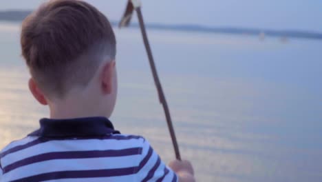 Caucasian-boy-in-a-striped-vest-on-the-waterfront.-Joyful-in-the-background-yachts,-sunset.