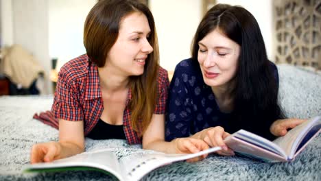 Two-young-woman-friends-are-watching-magazine-on-bed-in-bedroom-at-home