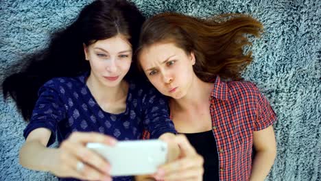 Top-view-of-two-pretty-girls-in-pajamas-making-selfie-portrait-on-bed-in-bedroom-at-home