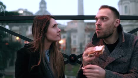 Pareja-joven-atractiva-tiene-una-rotura-en-el-centro-de-la-ciudad.-Hombre-y-la-mujer-sentada-en-la-noche-al-aire-libre,-comiendo-bocadillos