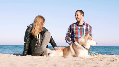 Joven-pareja-caucásica-en-la-playa-con-perro-husky-siberiano