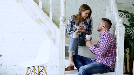 Glückliche-und-liebevolle-Pärchen-trinken-Tee-und-sprechen-beim-Sitzen-auf-der-Treppe-im-Wohnzimmer-zu-Hause