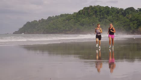 Slow-motion-shot-of-two-women-running-on-beach.