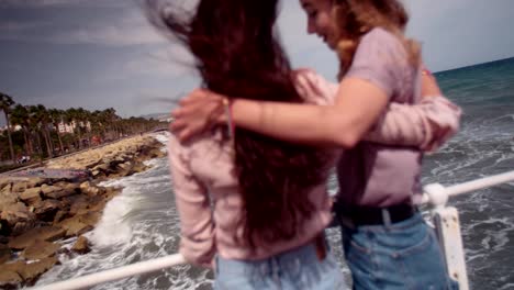 Young-female-friends-standing-on-jetty-embracing-and-discussing