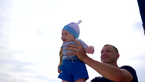 daddy-raised-baby-in-arms,-little-kid-in-father's-strong-hands-in-sunlight,-child-into-hands-of-dad-on-blue-sky-background