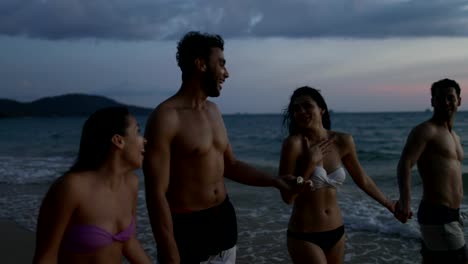 Grupo-de-amigos-hablando-en-la-playa-al-atardecer-POV,-gente-joven-sonriente-feliz-junto-al-mar-a-pie-durante-las-vacaciones-de-verano-en-el-mar