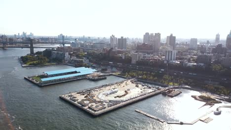 Vista-aérea-del-puente-de-Brooklyn-por-el-East-river-al-distrito-de-Brooklyn.-Drone-volando-sobre-el-muelle-en-la-orilla