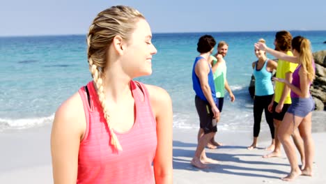 Fit-mujer-sonriendo-a-cámara-mientras-amigos-interactuar-detrás-de-ella-en-la-playa