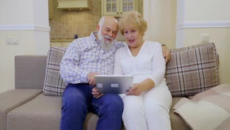 Ältere-Frau-und-senior-Mann-nutzt-Tablet-entspannend-am-Sofa-zu-Hause