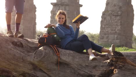 Los-turistas-de-backpacker-joven-feliz-estar-acostado-en-un-tronco-de-registro-lectura-libro-frente-antiguo-acueducto-romano-ruinas-en-el-Parque-parco-degli-acquedotti-en-Roma-al-amanecer-pareja-romántica-lenta