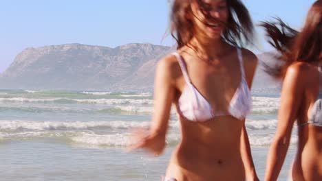 Female-Friends-Have-Fun-Running-Through-Waves-On-Beach-Vacation