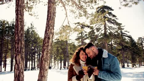 Couple-embracing-and-drinking-hot-beverage-on-snowy-winter-day