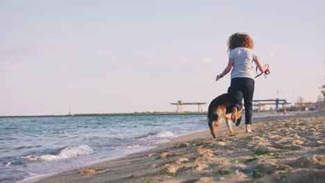 Mujer-joven-feliz-corriendo-y-jugando-con-su-perro-pastor-alemán-al-aire-libre-en-la-playa,-cámara-lenta