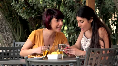 Dos-mujeres-hablando-y-utilizando-Smartphone-sentado-en-Cafe---amistad,-chisme,-conversaciones