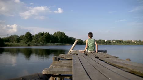 Junge-sitzt-auf-dem-Pier-und-schaut-etwas