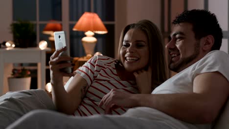 Young-family-using-phone-with-internet-in-bedroom