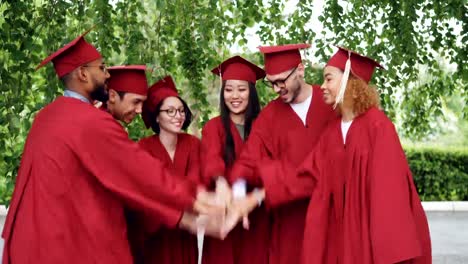 Glücklich-Graduierenden-Studenten-multiethnische-Gruppe-ist-Handflächen-zusammen,-dann-klatschenden-Händen-feiert-erfolgreichen-Abschluss,-Leute-Kleider-und-Mörtel-Boards-tragen.