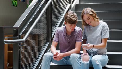 Estudiantes-de-secundaria-hombres-y-mujeres-sentados-en-las-escaleras-mirando-mensajes-en-el-teléfono-móvil