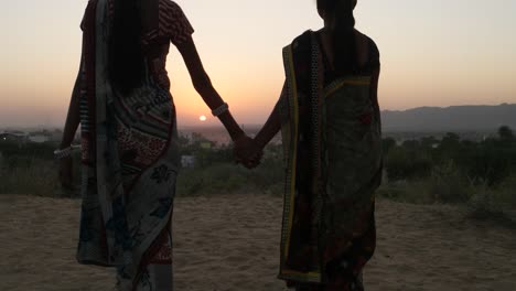 Dos-mujeres-stand-Mantenga-las-manos-en-ambiente-romántico-mirador-hermosa-puesta-de-sol-amanecer-alto-amplia-panorámica-surrealista-los-amantes-en-la-silueta-del-traje-tradicional-en-Rajasthan-India-mano-detrás-medio-dos