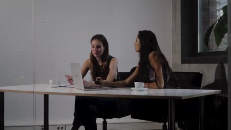 Las-mujeres-jóvenes-sentados-al-lado-hablando-en-un-entorno-de-oficina