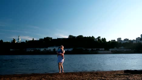 Schöne-blonde-Mutter-und-Tochter-führen-zueinander-auf-dem-River-Bank-bei-Sonnenuntergang.